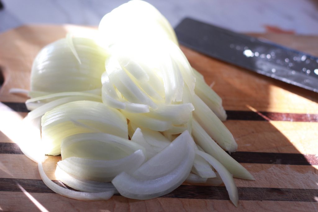 sliced onions on cutting board with knife in background