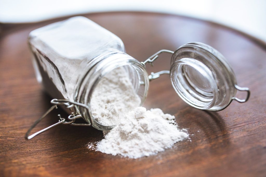 glass jar of flour on side with some flour spilling out onto table